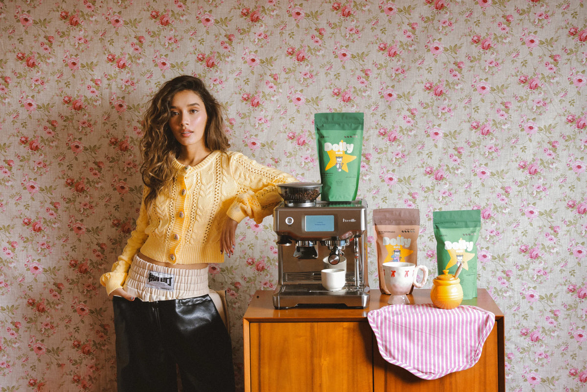 Mujer con suéter amarillo junto a la máquina de espresso y las bolsas de café Dolly